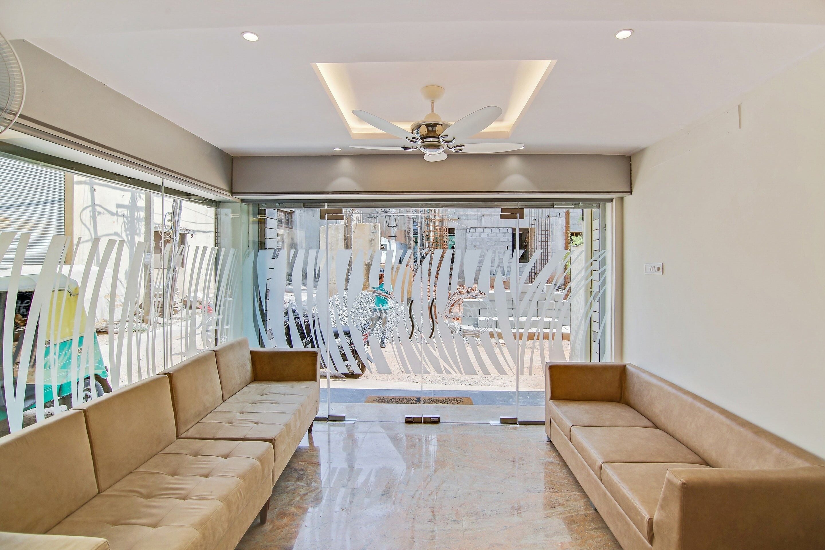 A modern interior with a ceiling fan, a glass partition with vertical slats, and a beige sofa.