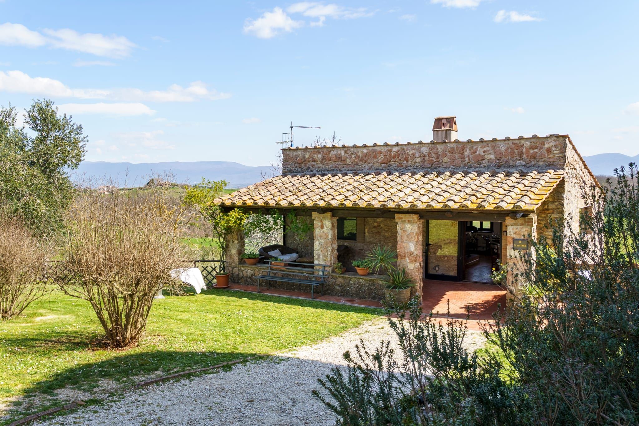 Une maison en pierre avec un toit en tuiles, un chemin de gravier et une zone herbeuse plantée.