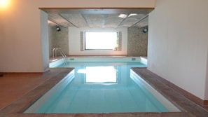 An indoor swimming pool with a view of a window and a stone wall.