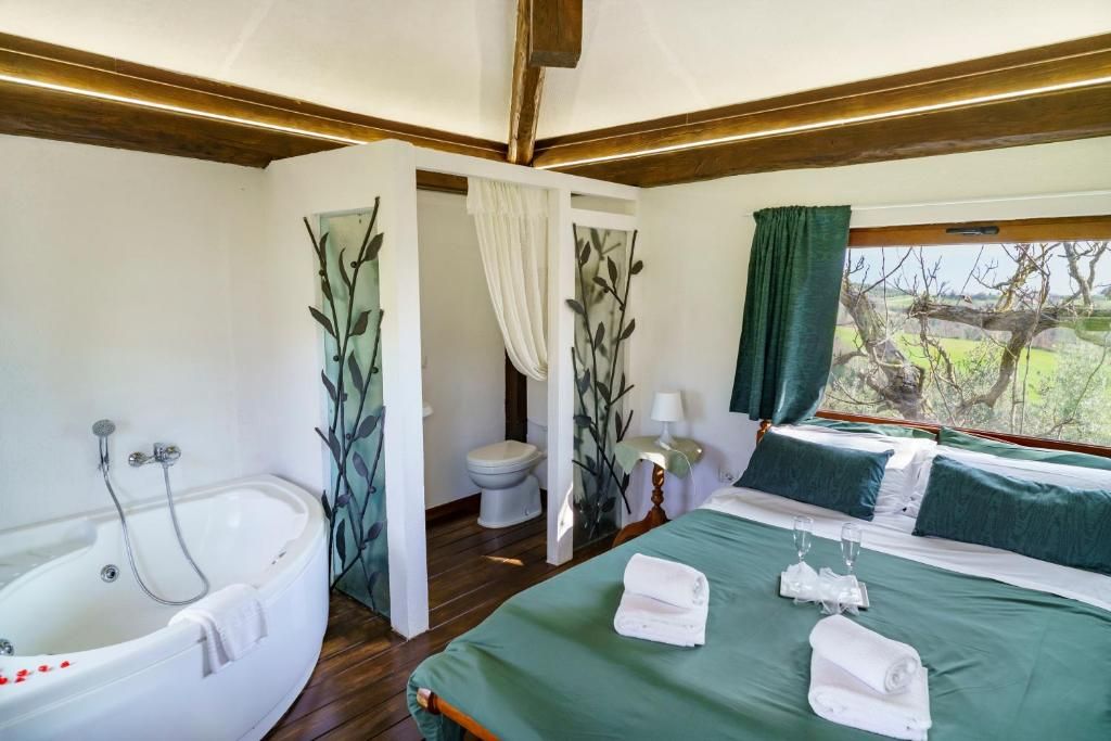 A room with a large bed, a bathtub, and a window with a view of trees.