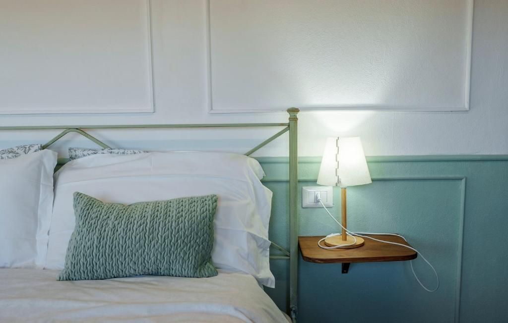 Una cama con sábanas blancas y un almohadón verde, una mesita de noche con una lámpara, y una pared con diseño de panel.