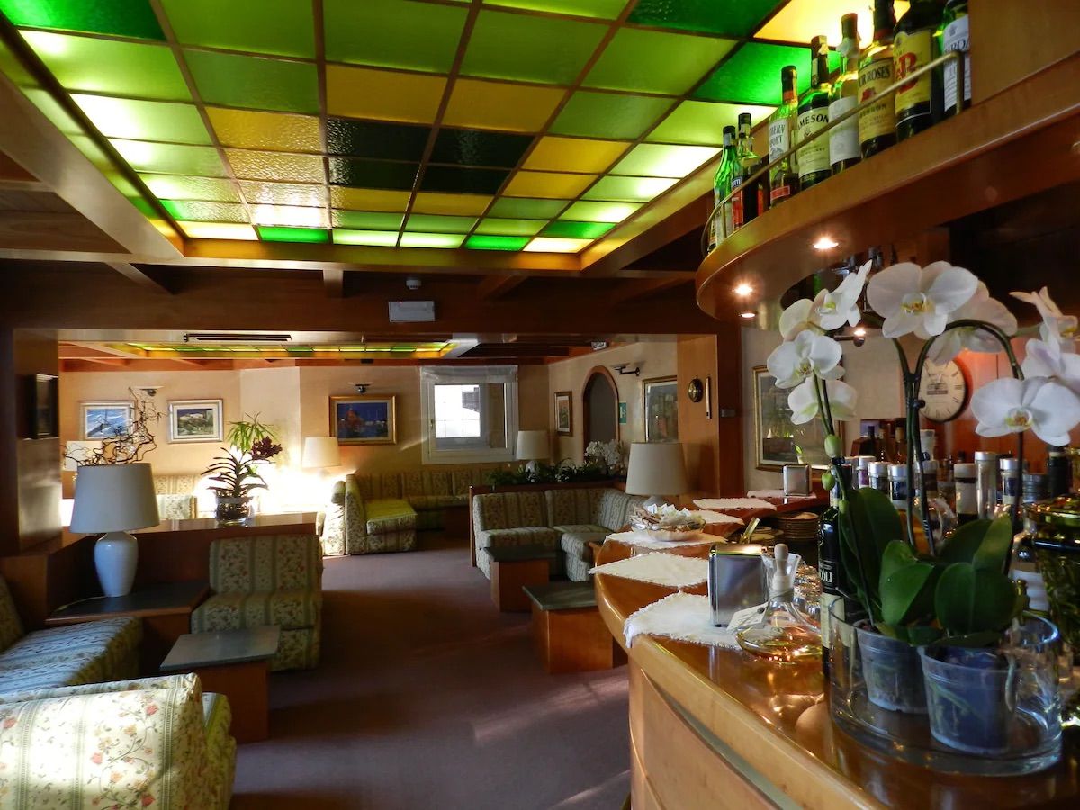 Un vestíbulo de hotel con techos altos, varias zonas de estar y un bar con diferentes botellas.
