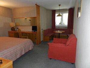 Habitació d'hotel amb un llit, escriptori, cadira, taula petita i un sofà.