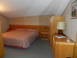 Habitació d'hotel amb llit, taulella de nit, làmpada i una petita taula amb cadira.