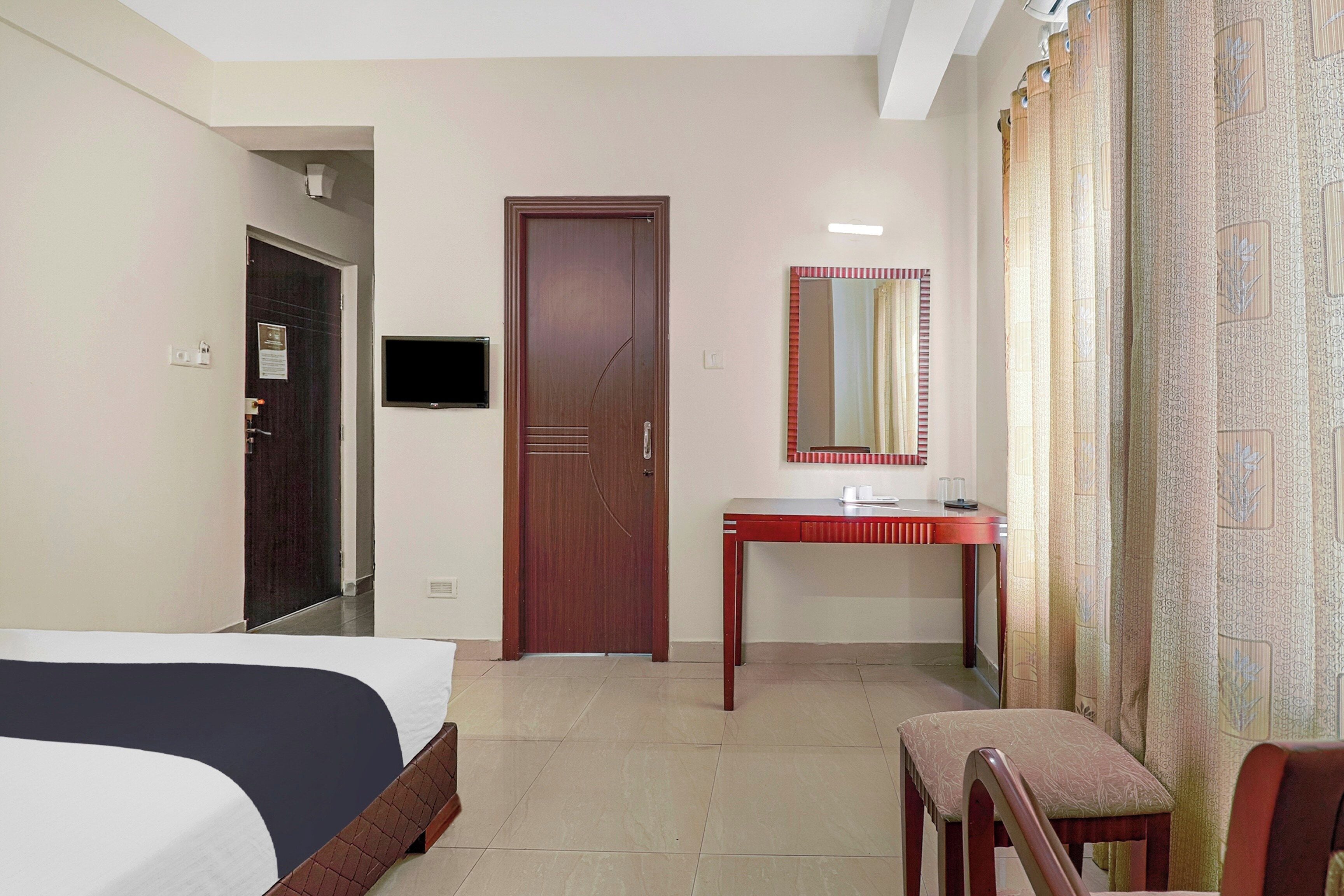 Una habitación de hotel con cama, escritorio, silla, espejo y puerta.