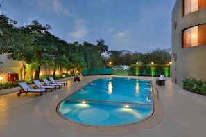 A swimming pool with lounge chairs, surrounded by greenery and a building with large windows.
