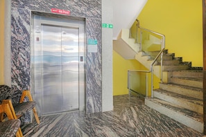 An elevator with a digital display, a fire exit sign, and a staircase with metal railings. - Collection O 29 Church's Inn Near Cubbon (Bangalore)