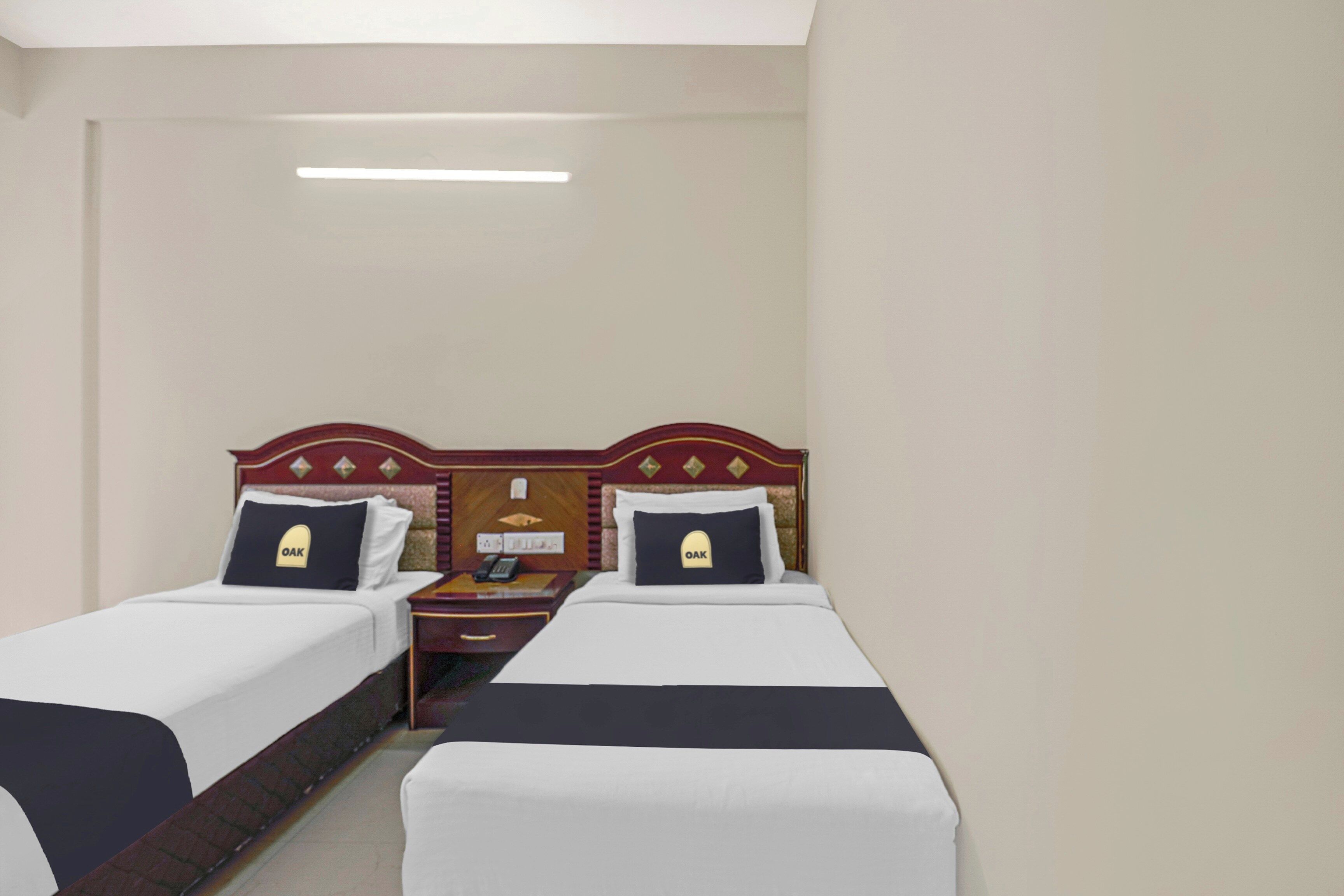 A hotel room with two single beds, a wooden headboard, a nightstand with a phone, and a wall-mounted light.