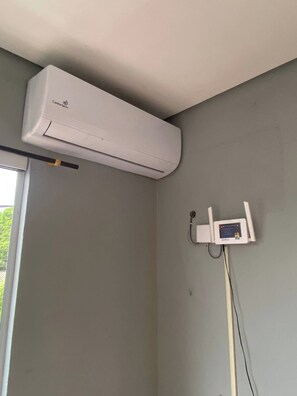 Una habitación con un equipo de aire acondicionado blanco montado en la pared y un pequeño dispositivo electrónico adherido a la pared cerca de una ventana.