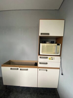 Una kitchenette con un microondas, un refrigerador pequeño y un armario de madera.