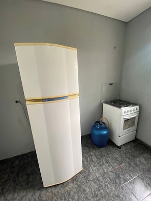 A kitchen with a white refrigerator, a gas stove, and a blue gas cylinder.