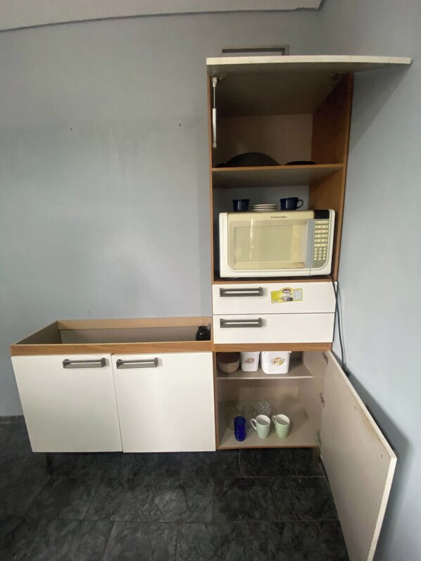 Una kitchenette con microondas, armarios de almacenamiento y una encimera.