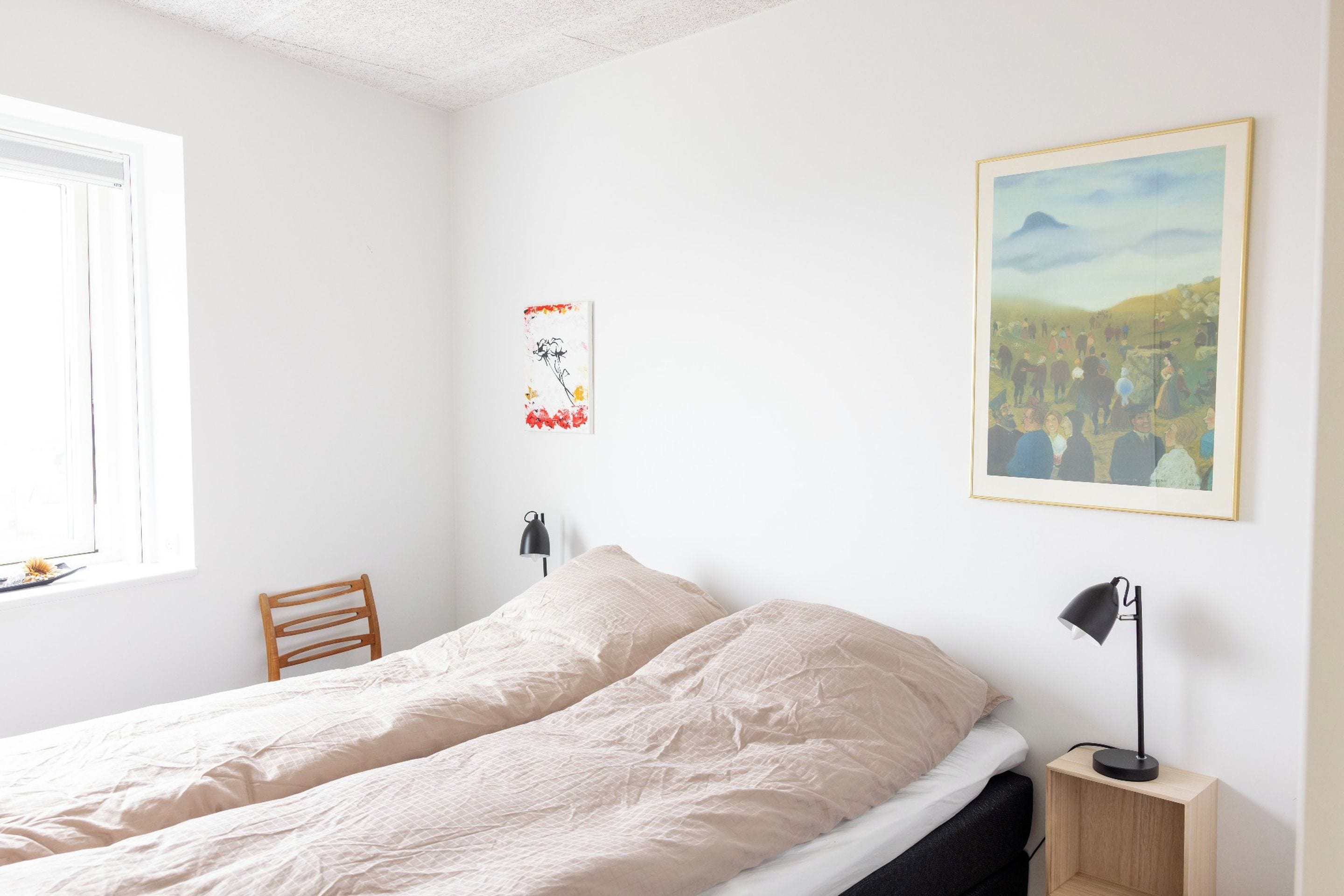 A bedroom with a bed, a chair, a nightstand, a lamp, and two wall-mounted artworks.