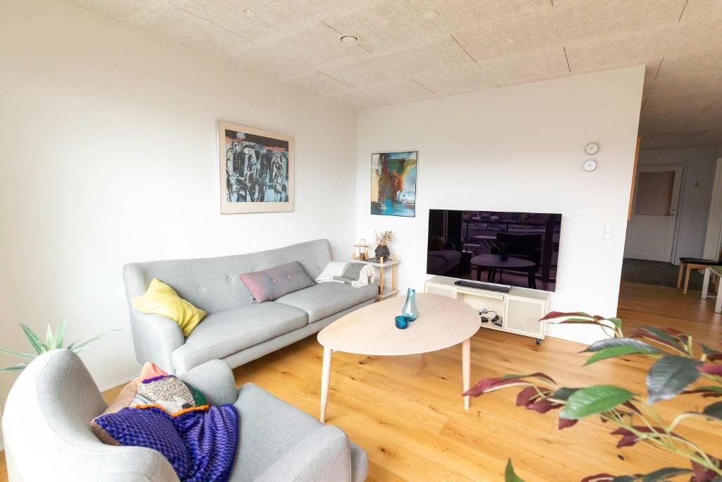 Una sala de estar moderna con un sofá gris, una mesa de centro, un televisor de pantalla plana y un comedor al fondo.