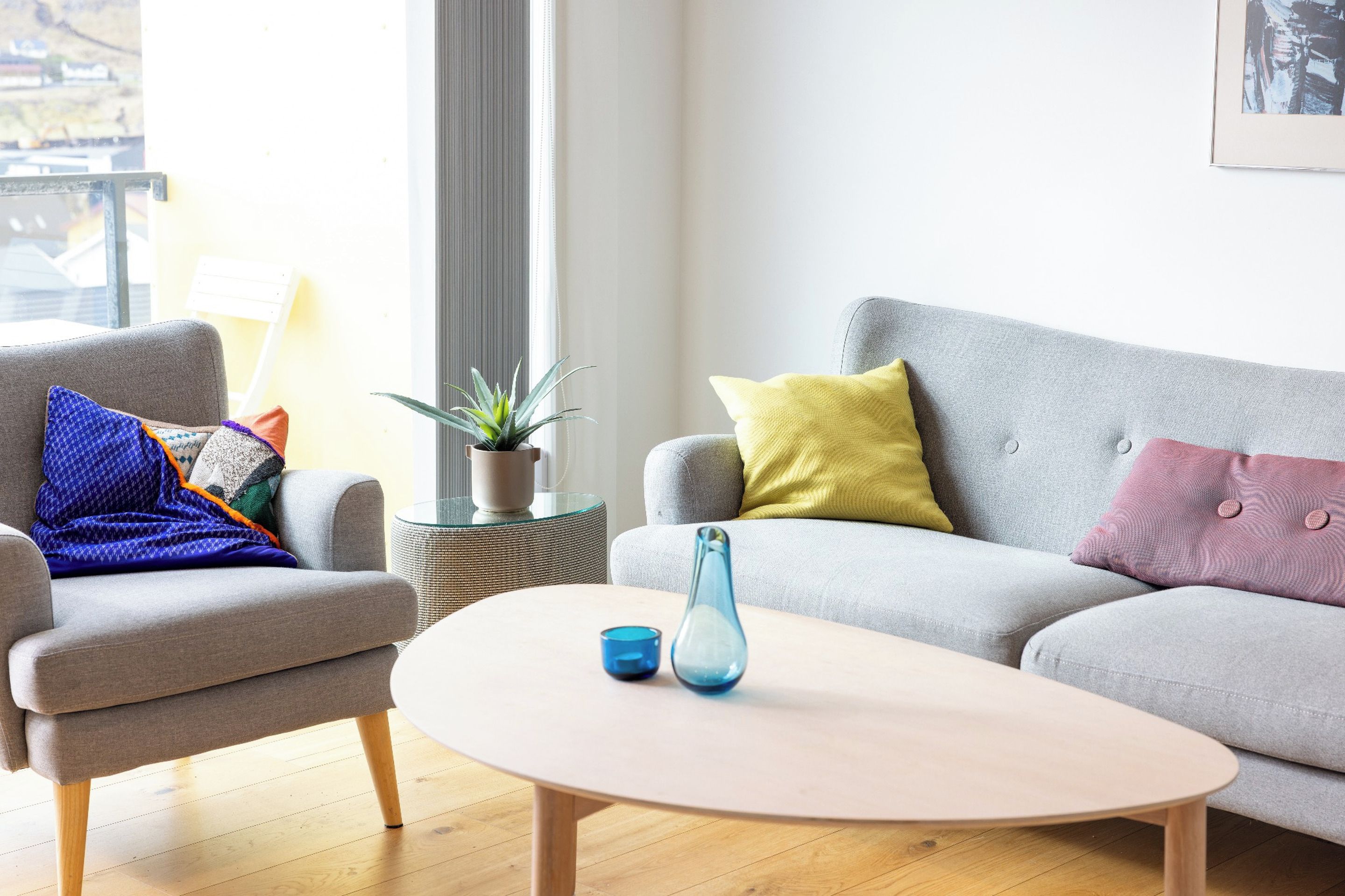 A modern living room with a grey sofa, a grey armchair, a round coffee table, and a potted plant.