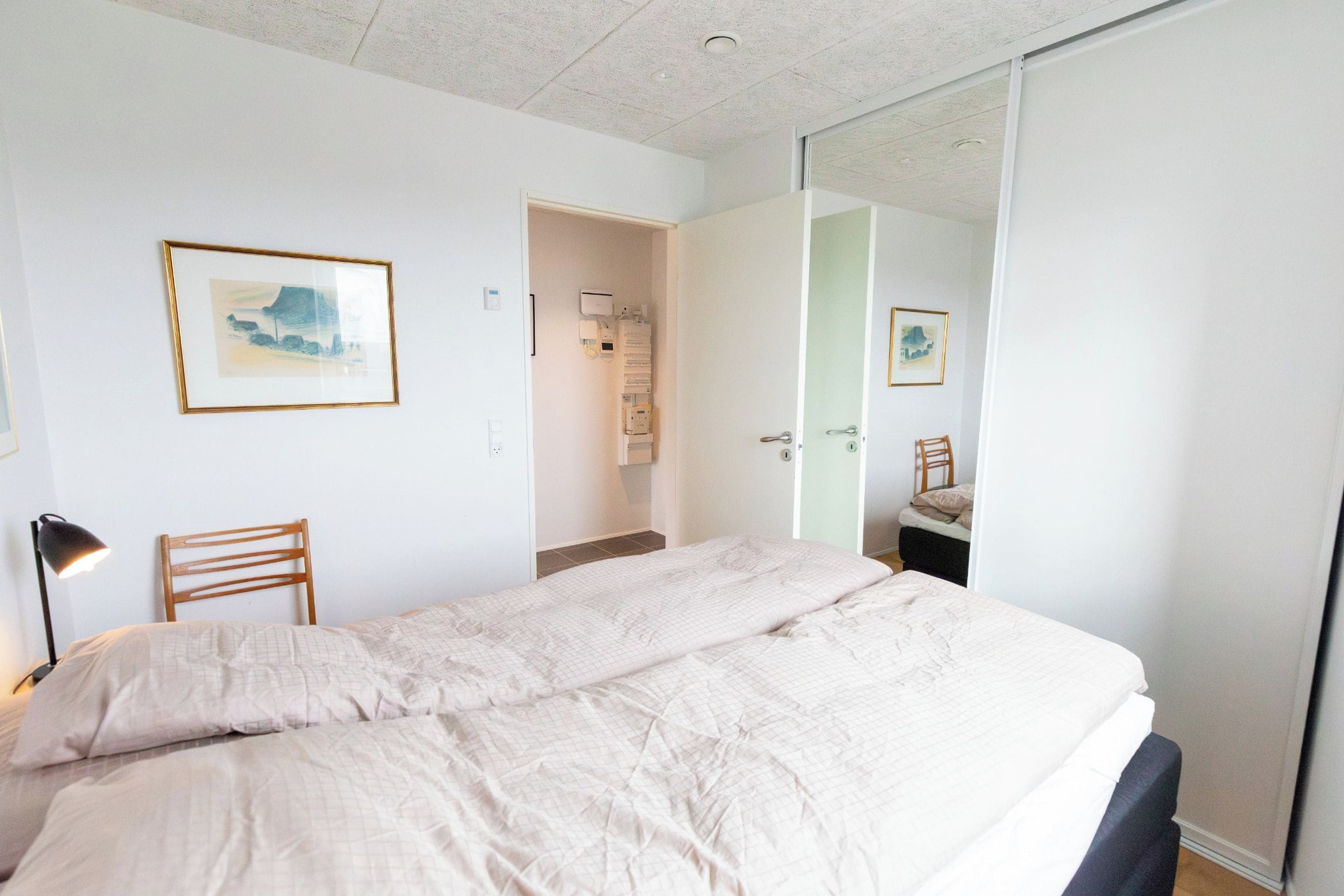 A bedroom with a bed, a chair, a desk, a mirror, and a door leading to a bathroom.