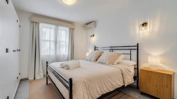 Habitació d'hotel amb llit, taulell de nit, làmpada, aparell d'aire condicionat i cortines.