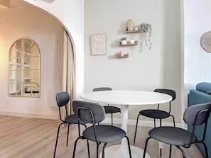 A dining area with a round table and six chairs, a wall-mounted shelf with decorative items, and a large window with curtains. - Apartment for 6 people near the sea in Toulon (Toulon)