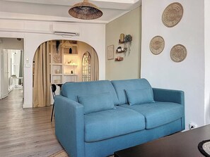 A living room with a blue sofa, decorative wall art, and a hallway leading to a kitchen. - Apartment for 6 people near the sea in Toulon (Toulon)