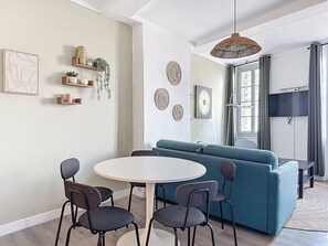 Moderni olohuone, jossa on pyöreä ruokapöytä, neljä tuolia, turkoosi sohva ja koristeellinen seinätaideteos.