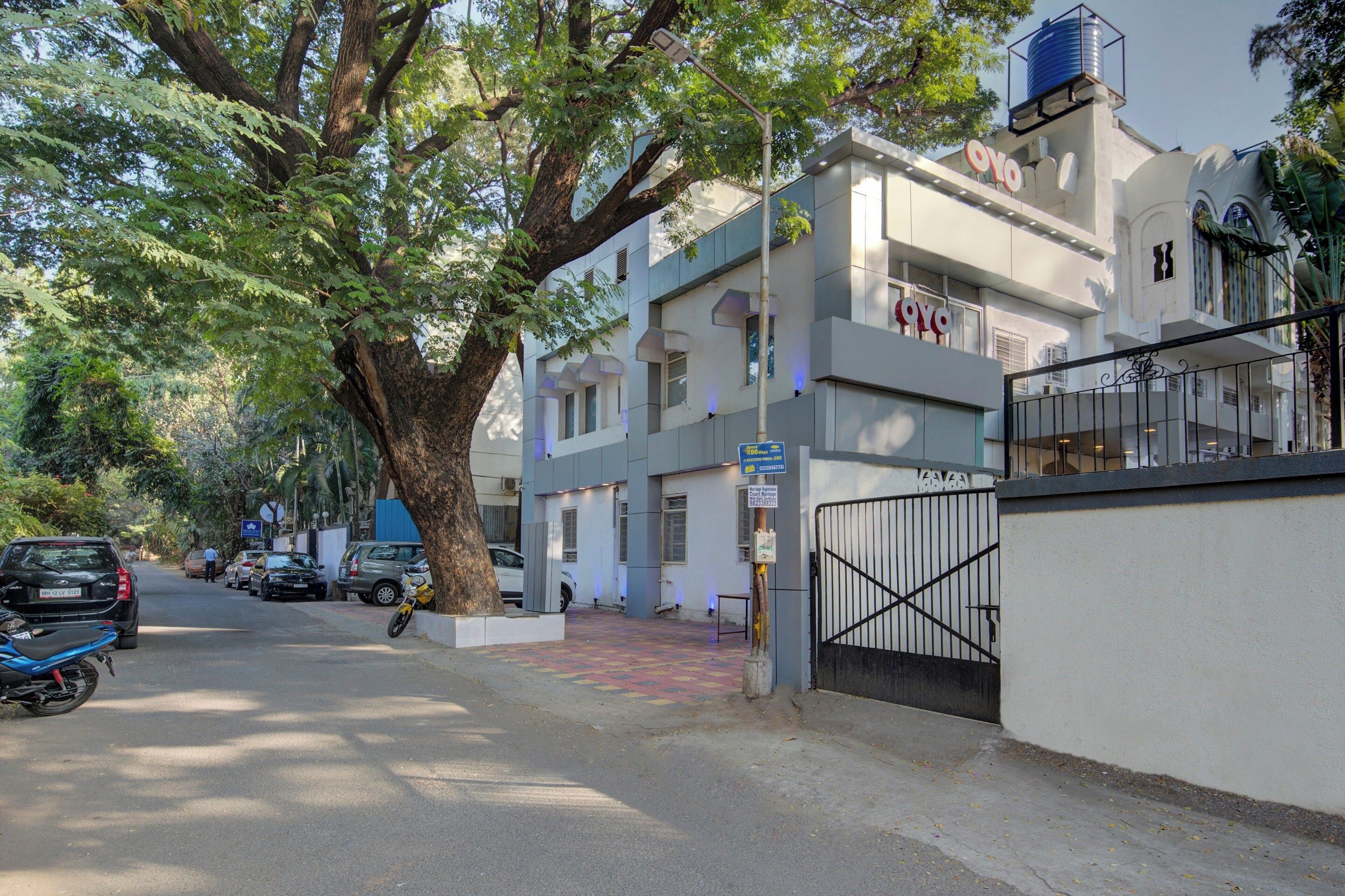 A multi-story building with a gated entrance, parked vehicles, and a tree-lined street.