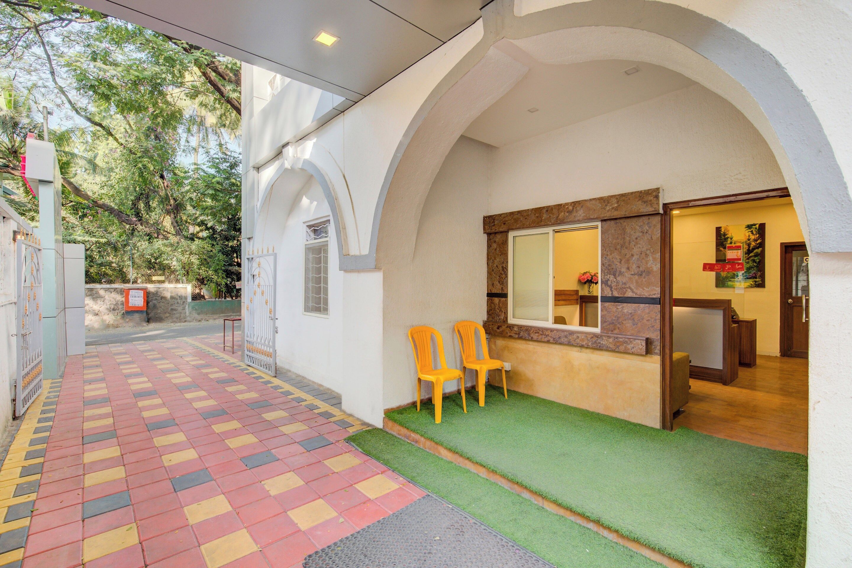 L’entrée d’un hôtel, avec un trottoir dallé, un comptoir d’accueil et deux chaises à l’extérieur.