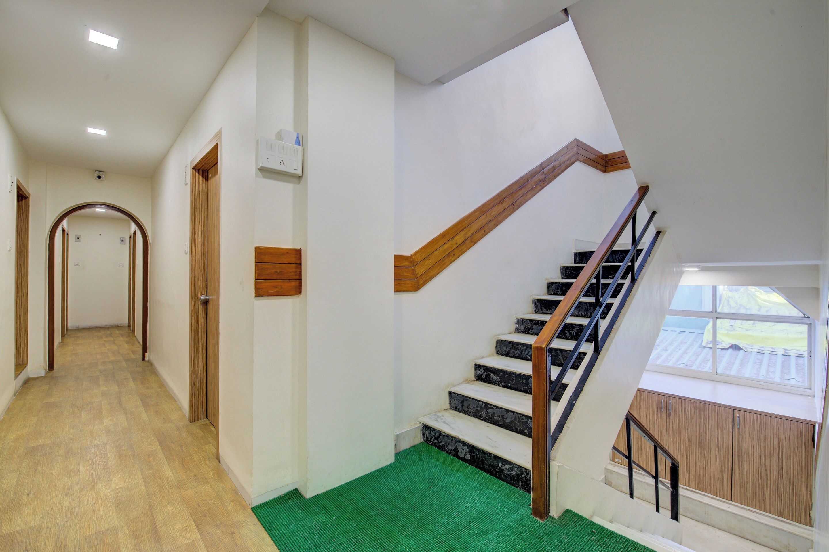 A staircase with wooden handrails and black steps, leading to a landing with a green mat.