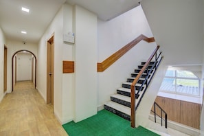 A staircase with wooden handrails and black steps, leading to a landing with a green mat. - Super Collection O Sunshine Near Inox (Pune)