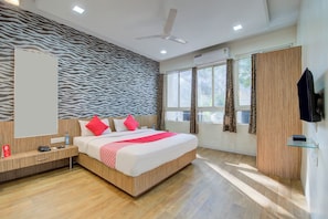 A modern hotel room with a zebra-patterned wall, a large bed with red and white bedding, a wooden floor, a ceiling fan, and a TV mounted on the wall. - Super Collection O Sunshine Near Inox (Pune)