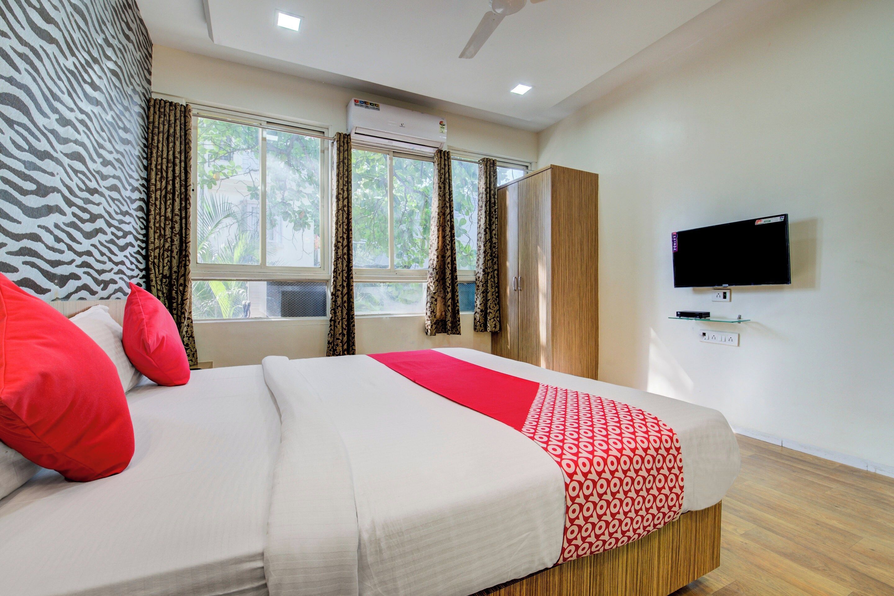 A hotel room with a bed, curtains, a television, and an air conditioning unit.