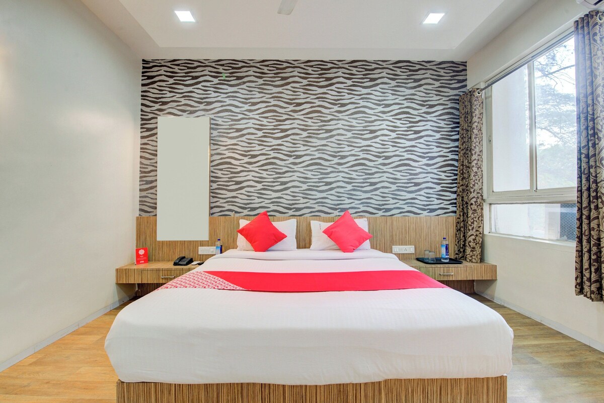 A hotel room with a large bed, a zebra-patterned wall, a window with curtains, and a wooden floor.