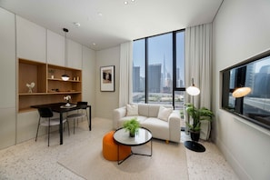A modern living room with a sofa, a dining table, and a coffee table. There is a large window with a view of a city skyline. - Chic Studio in Upside Living Burj Khalifa View (Dubai)