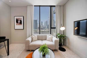 A modern living room with a sofa, a coffee table with a plant, a framed picture on the wall, and a view of a city skyline through large windows. - Chic Studio in Upside Living Burj Khalifa View (Dubai)