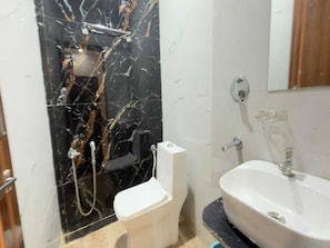 A bathroom with a black marble shower wall, a white toilet, and a white sink with a mirror above it. - Classic Hotel C&D Stay (Indore)