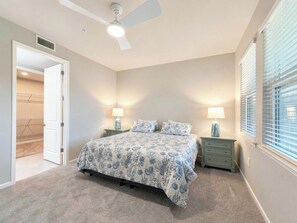 Un dormitorio con cama, mesitas de noche, ventilador de techo y ventana con persianas.