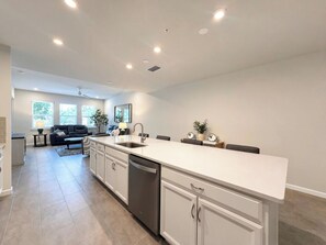 A modern kitchen with a central island, built-in appliances, and a dining area with a sofa and table. - Resort-Style Naples Escape | Arboretum Pool & Spa | Near Downtown (Naples)