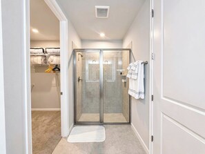 Un baño moderno con cabina de ducha de vidrio, un perchero y un espacio de almacenamiento visible con cestas.
