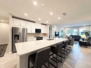 A modern kitchen with a large island, stainless steel appliances, and a dining area with bar stools. - Resort-Style Naples Escape | Arboretum Pool & Spa | Near Downtown (Naples)