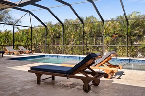 A pool area with lounge chairs and a glass-enclosed structure. - Coral Breeze Retreat (Cape Coral)