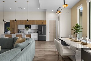 A modern kitchen with a central island, a dining area with a long table, and a living room with a sofa. - Terra Cove | Heated Pool, Dock & Gulf Access (Cape Coral)