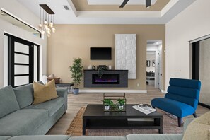 A modern living room with a fireplace, a sofa, a coffee table, and a blue armchair. - Terra Cove | Heated Pool, Dock & Gulf Access (Cape Coral)
