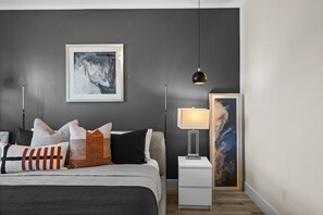 A modern bedroom with a bed, pillows, a bedside table, a lamp, and artwork on the wall. - Terra Cove | Heated Pool, Dock & Gulf Access (Cape Coral)
