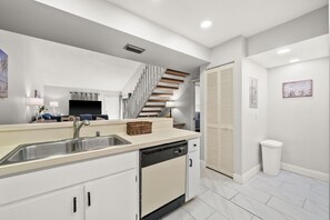 A modern kitchen with a dishwasher, a sink, and a staircase leading to another level. - Sunny Fort Myers 2BR Condo | Pool & Hot Tub (Fort Myers)