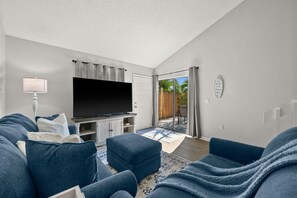 Ein Wohnzimmer mit Flachbildfernseher, einer Couch, einem Hocker und einem Couchtisch.