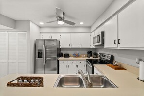 A modern kitchen with stainless steel appliances, white cabinets, and a ceiling fan. - Sunny Fort Myers 2BR Condo | Pool & Hot Tub (Fort Myers)