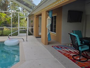 Ein überdachter Außenbereich mit Pool, Stuhl und einem gemusterten Teppich.