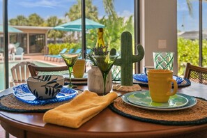 A table set with a bowl, a bottle, a cactus, and a mug, with a view of a pool and palm trees. - Punta Gorda Isles| Optional Guest  House (Punta Gorda)