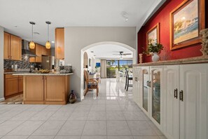 A modern kitchen with wooden cabinets, a central island, pendant lighting, and a dining area with chairs and a table. - Punta Gorda Isles| Optional Guest  House (Punta Gorda)