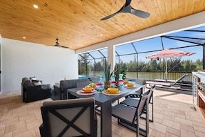 Eine Terrasse im Freien mit einem Esstisch für vier Personen, umgeben von Stühlen und einem Deckenventilator.