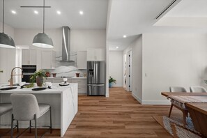 Cozinha moderna com ilha central, eletrodomésticos de aço inoxidável, iluminação pendente e piso de madeira.